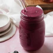 The banana berry smoothie is in a mason jar with a glass straw.