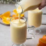 The orange banana smoothie is being poured into a glass with a small handle.