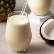 In the background is a large pineapple and a glass straw is in the glass with the coconut pineapple smoothie.