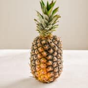 A pineapple is standing by itself on a white board.