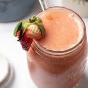 A strawberry banana smoothie without milk is in a mason jar garnished with a strawberry and a glass straw is in the mason jar.