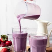A hand is pouring the blackberry strawberry smoothie into a glass.