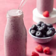 The smoothie is next to a bowl with blueberries and a bowl with raspberries.