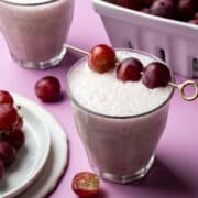 Three grapes are skewered on a gold toothpick that is placed over a glass.