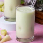 A honeydew smoothie is in front of another honeydew smoothie that is on a big white puck.