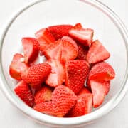 A bowl of frozen strawberries is in a bowl on a white background.