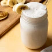 A banana milkshake is in a mason jar with a glass straw out of the glass.
