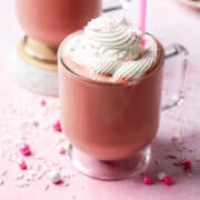 A cherry chocolate milkshake is topped with whipped cream on a pink background.