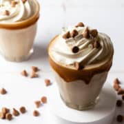 A peanut butter milkshake is on a white puck surrounded by peanut butter chips.