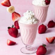 A skewer with pieces of strawberries and bananas are garnishing a strawberry banana milkshake.