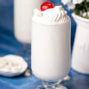 A cherry is topping a frozen white hot chocolate in a large glass.