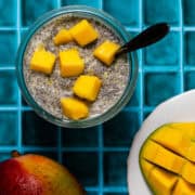 A spoon is in a jar of mango chia seed pudding topped with cut up pieces of mango.