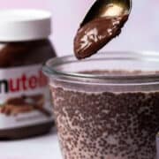 A spoon is adding Nutella to a chia seed pudding bowl.