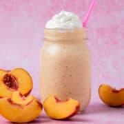 Pieces of peaches are surrounding the peach milkshake.
