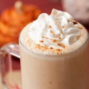 The pumpkin spice milkshake is topped with whipped cream and sprinkled with ground cinnamon in a glass that has a handle.