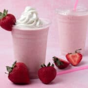 The strawberry milkshake is topped with whipped cream and there are strawberries scattered around the base of the milkshake.