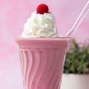 The whipped cream is topped with a raspberry that is on top of a raspberry milkshake.
