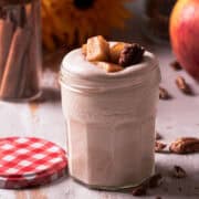 An apple cinnamon mousse is in a small jar surrounded by sunflowers and apples.