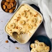 A serving of the banana pudding is taken out of the pan and placed in a bowl next to the pan.