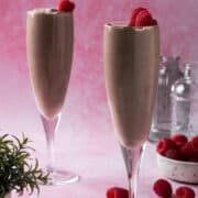 Two champagne flutes are full of chocolate mousse and topped with raspberries.