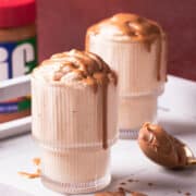 Two glasses of peanut butter mousse are topped with peanut butter and it is dripping off of the sides of the glasses.