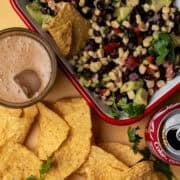 The avocado black bean salsa is in a square dip surrounded by chips and sodas.