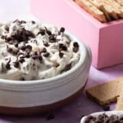 The cannoli dip is in a large bowl next to a square pink box with graham crackers.