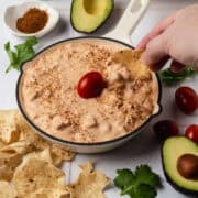 A hand is dipping a chip into the skillet filled with the cold taco dip.