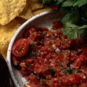The cherry tomato salsa is in a serving bowl with the cilantro overhanging the bowl.