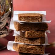 The no bake gingerbread bars are stacked on top of each other lined with parchment paper.
