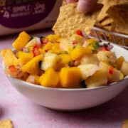 A chip is being dipped into the pineapple mango salsa.