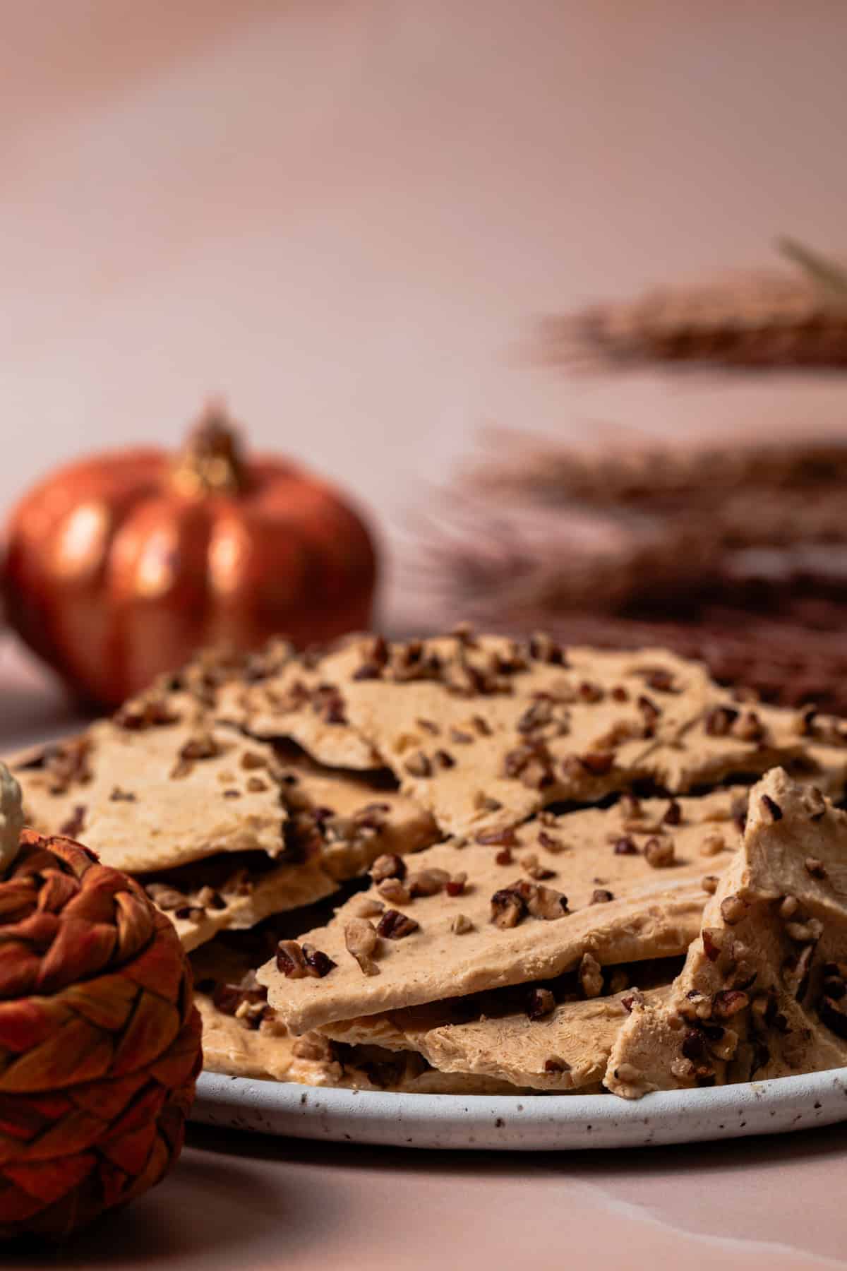 A pumpkin is behind a plate full of pumpkin spice yogurt bark.