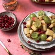The maple pecan fruit salad is on a plate surrounded by pomegranate seeds.