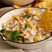 A chip is in the bowl of Mexican street corn dip.