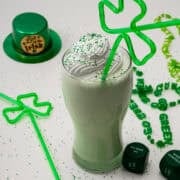 The shamrock milkshake is in a glass with a shamrock straw outside surrounded by a green hat.