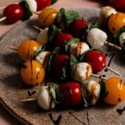 Six caprese skewers are on a circular cutting board drizzled with balsamic vinegar.