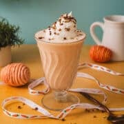 Ribbon is surrounding the glass of the carrot cake milkshake on an orange background.