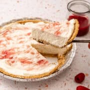 A slice of the no bake raspberry cheesecake is lifted over the full pie.