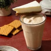 A cheesecake slice is on top of the cheesecake milkshake.