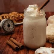 The cinnamon roll milkshake is in a mason jar topped with whipped cream and a cinnamon stick.