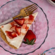 A fork is on a plate with a slice of the no bake strawberry cheesecake pie with a strawberry on the plate garnishing it.