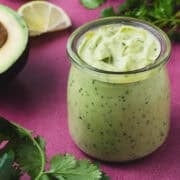 The avocado cilantro dressing is next to slices of lime and an avocado cut in half.