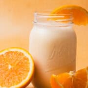 A creamsicle milkshake is poured into a mason jar with slices of oranges around the mason jar.