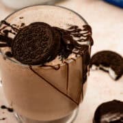 Oreos and a chocolate drizzle top a glass filled with the Oreo milkshake.