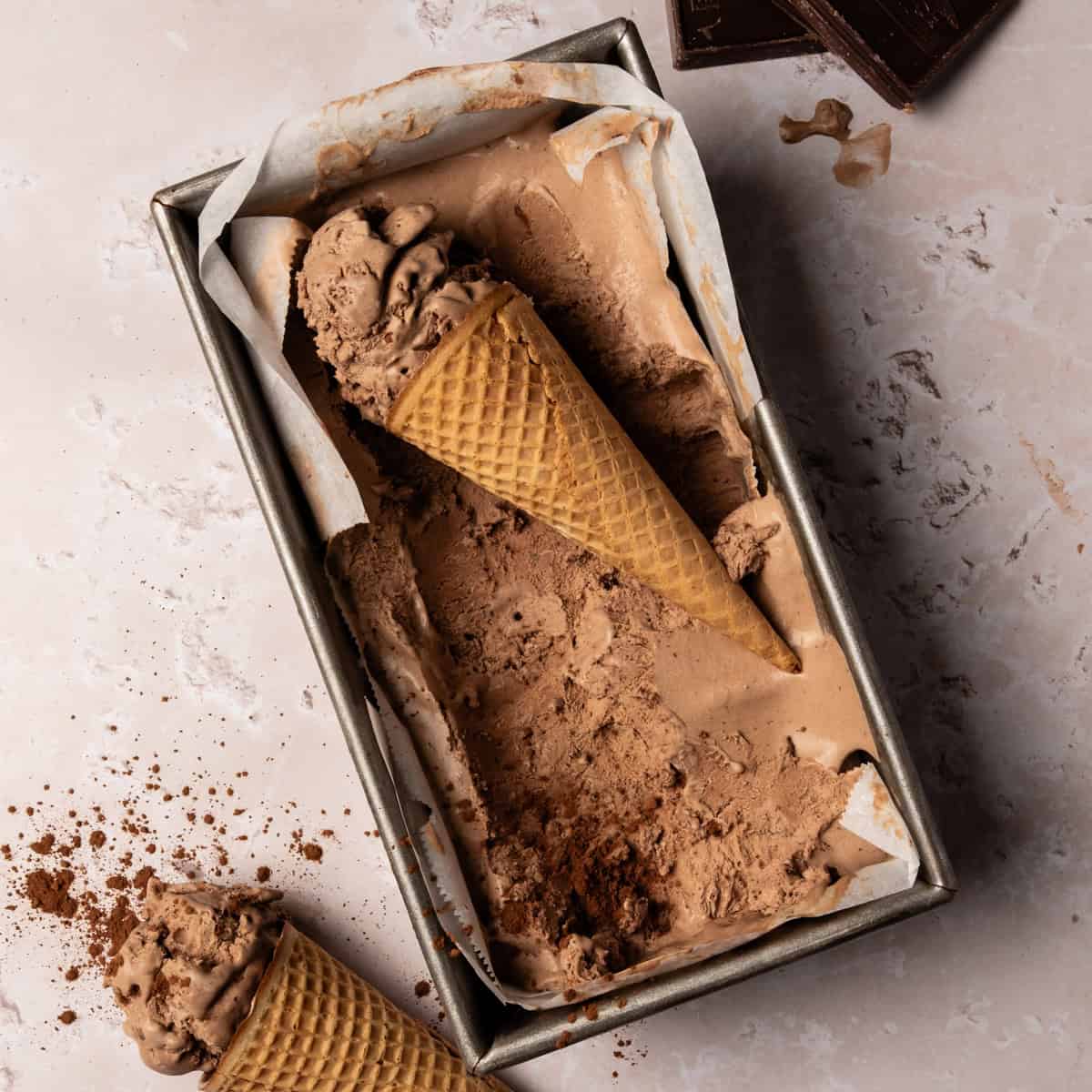 An ice cream cone is laying in the loaf pan with the no churn chocolate ice cream in the loaf pan.