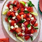 The watermelon feta salad is on an oval plate surrounded by slices of watermelon.