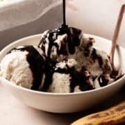 Chocolate sauce is being poured onto a bowl of banana ice cream.