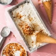 The no churn coconut ice cream is in a loaf pan with one cone in a loaf pan and one next to it.