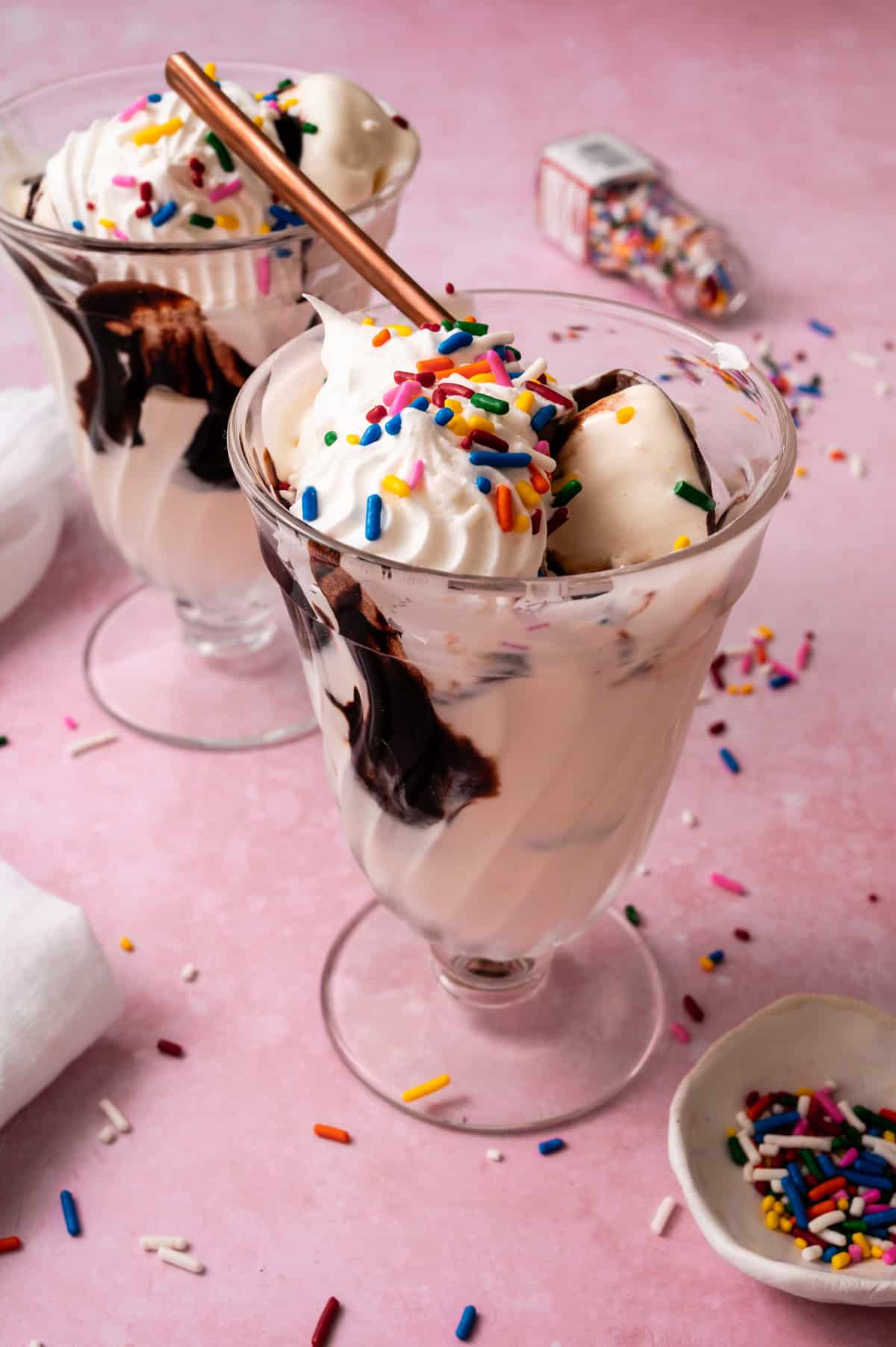 A spoon is in the cup with the ice cream topped with sprinkles.