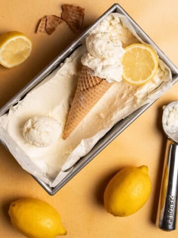 Two full lemons are next to the lemon loaf pan and has an ice cream scoop next to it.